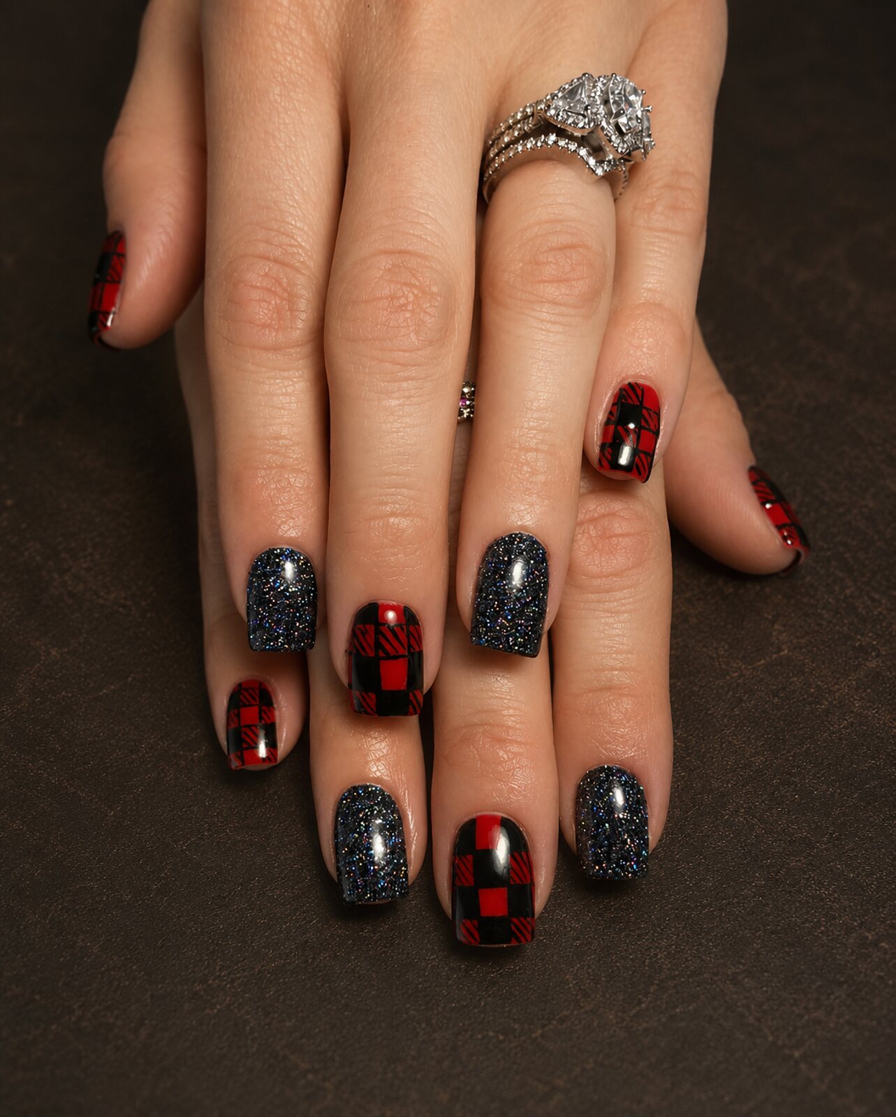 Hands with short square nails in red and black check with dark glitter accents
